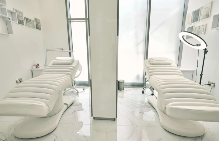 Cream electric facial bed with a white rolling stool and ring light in a bright beauty treatment room