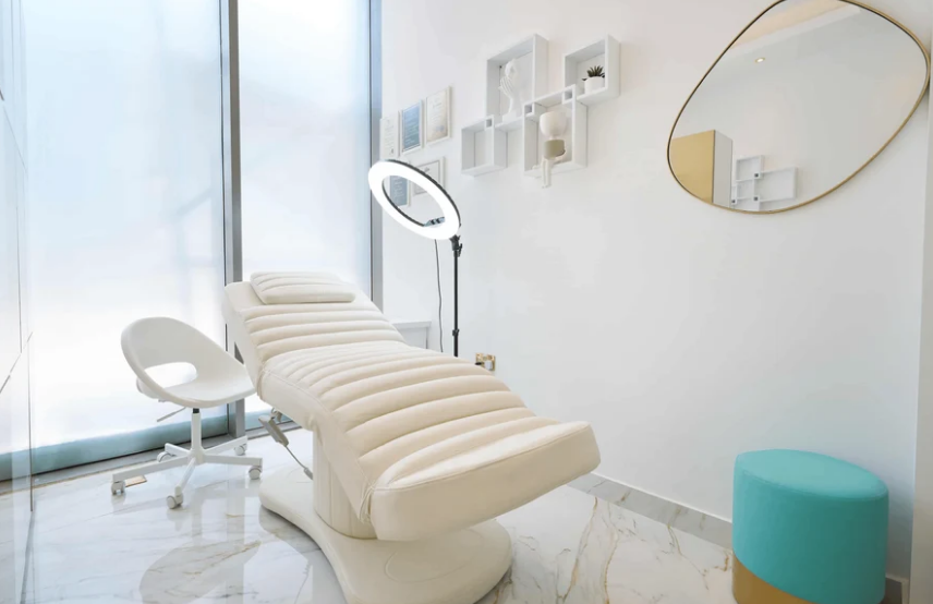 Cream electric facial bed with a white rolling stool and ring light in a bright beauty treatment room